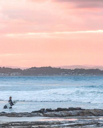 A surfer making his way back to the break after a long ride to shore at sunset.の写真素材