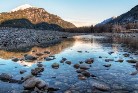 Clear river with rocks leads towards mountains lit by sunsetの写真素材