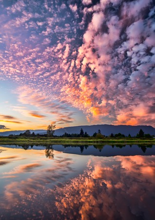 Reflection of dramatic pink clouds in waterの写真素材