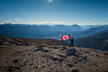Woman holding a Canadian flag in the Canadian Rocky Mountains (Rockies) in Jasper National Park, Alberta, Canada.の写真素材