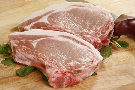 two uncooked pork chops on a wooden boardの写真素材