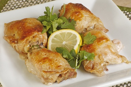 four roast chicken thighs with coriander and lemon on a white plateの写真素材