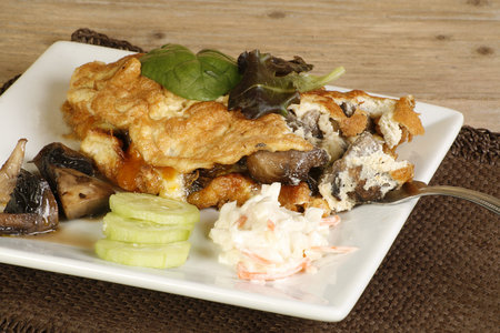 cheese and mushroom omelette with coleslaw mushrooms and cucumber on a wooden table