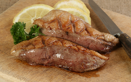 two cooked duck breasts with lemon and parsley on a chopping boardの写真素材