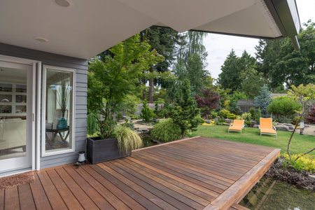 A perspective view of a contemporary Pacific Northwest home with a deck bridging a pond that leads to a pair of modern yellow loungers in a landscaped yard.の写真素材