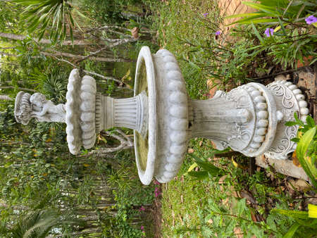 Cupids fountain in the garden against the background of the trees. Beauty and decor in vintage style. Stone fountain with marble statue of cupid in summer and green trees.の写真素材