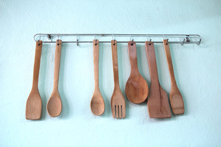 Kitchen utensil: wooden spoon, wooden fork and wooden spatula hang on white wall.