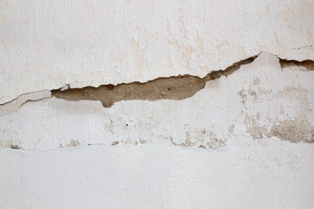 cracked concrete wall covered with old white surface as background