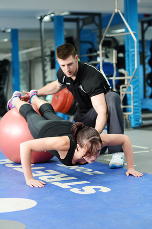 Personal trainer helping young woman in gymの写真素材