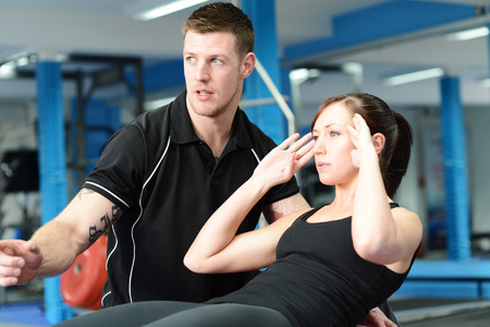 Personal trainer helping young woman in gymの写真素材