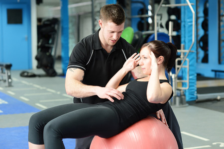 Personal trainer helping young woman in gymの写真素材