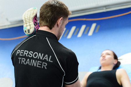 Personal trainer helping young woman in gym with stretching exercisesの写真素材