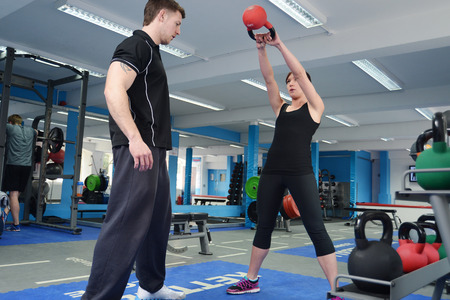 Young woman working out with kettle bell weights, with personal trainer in gymの写真素材