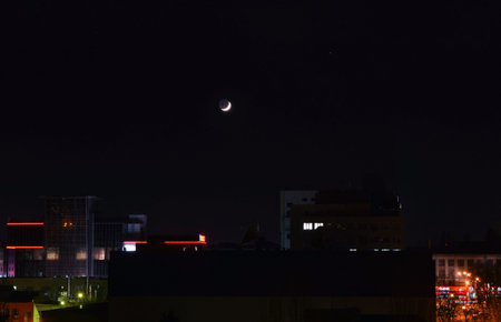  The young crescent moon over an evening city.