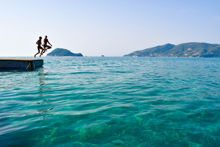Silhouettes of people on the pontoon jumping into the sea.の写真素材