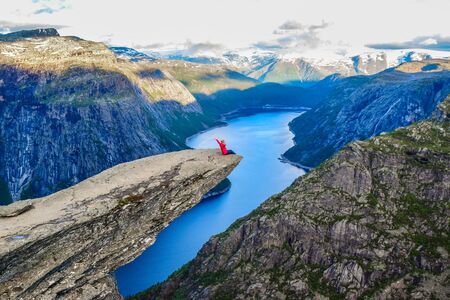 The girl sits on the edge of the cliff on the Trolltunga, Norway.の写真素材