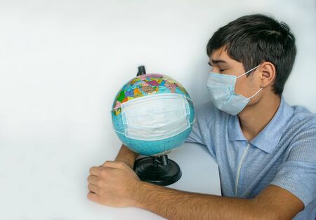 Guy and Earth globe in protective masks, as a symbol of the fact that people of entire planet are quarantined due to the epidemic and pandemic of Coronavirus. Copy space, banner or template.の写真素材