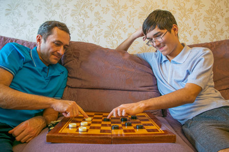 Dad and teenager son in protective masks play checkers, staying at home on self-isolation quarantine...