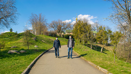 Father and son in protective medical masks walk through the park on a sunny spring afternoon. Safety...