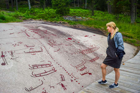 Tourists near rock carvings from Bronze Age, which are about 3000 years old. Located at one time on the shores of the fjord, now a UNESCO World Heritage Site. Tanum, Sweden.のeditorial素材