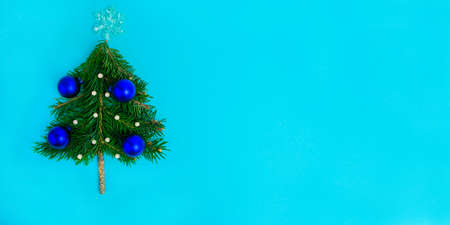 Small Christmas tree decorated with blue balls on turquoise background. Christmas and New Year minimalistic concept. Copy space, template for design, lettering or text. Flat lay.の写真素材