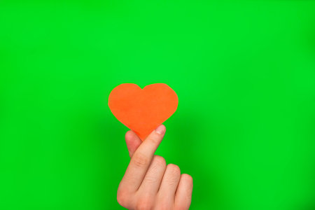 Guy's hand holding a red paper heart on greenの写真素材