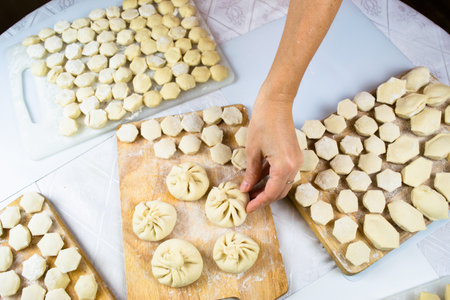 The woman's hands, soiled with flour, neatly lay out handmade, freshly made dumplings, ravioli and khinkali on cutting boards. Delicious homemade food. White background, close-up, selective focus.の写真素材