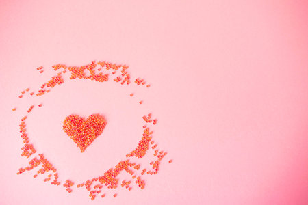 One red heart made of beads as a symbol of love on an isolated pastel light pink background....