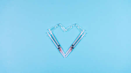 Syringes and ampoules for a vaccine in the shape of a heart on a light blue background.の写真素材