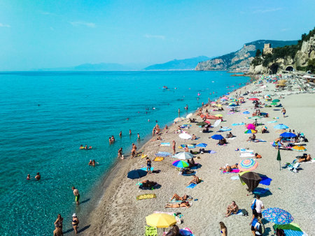 Finale Ligure, Italy - 23 july 2019: Vacationers on the free sandy and pebble Capo San Donato or Castelleto Pier Beach on a summer, sunny day near the calm Mediterranean Sea. Ligurian Riviera coast.のeditorial素材