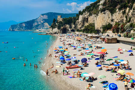 Finale Ligure, Italy - 22 july 2019: Vacationers on the free sandy and pebble Capo San Donato or Castelleto Pier Beach on a summer, sunny day near the calm Mediterranean Sea. Ligurian Riviera coast.のeditorial素材