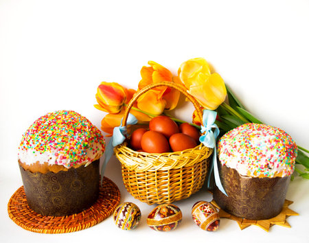 Easter cakes, a wicker basket decorated with blue ribbons with brown Easter eggs, bouquet of yellow...