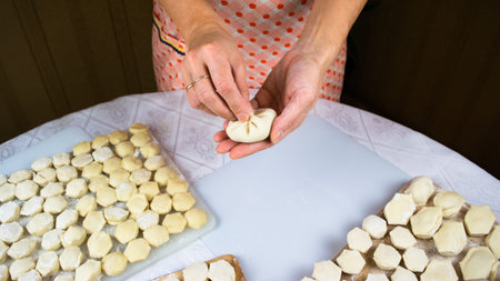 Woman's hands sculpt khinkale dumplings on background of cutting boards with hendmade dumplings,...