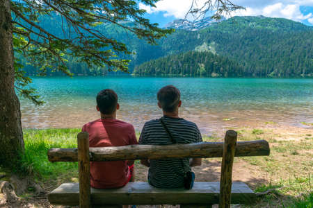 Tourists on a wooden bench near Glacial Black Lake. Premium tourist attraction of Durmitor National Park. Walking path circles around lake, and is a popular destination for recreation and hiking. Montenegroの写真素材