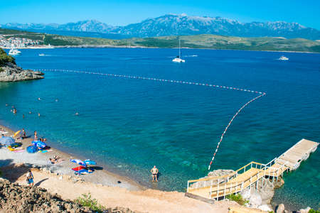 Velja Spila beach, Montenegro - June 28, 2021: Vacationers on the small pebble beach with clean water, located on Lustica peninsula of Trashte Gulf. Adriatic Sea. Summer sunny landscape.のeditorial素材