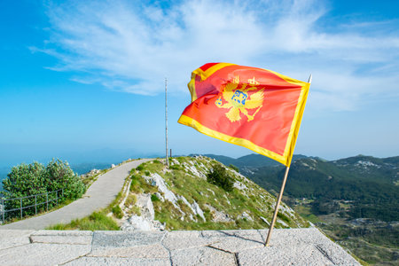 Waving flag of Montenegro against the background of viewpoint at top of Jezerski mountain, near Njegos mausoleum in Lovcen National Park. Montenegro. Summer blue mountain landscape.の写真素材