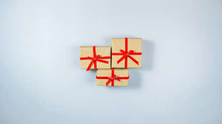 Three boxes wrapped in craft paper and tied with red ribbon in center on light gray background. Concept of holidays and gifts preparation. Flat lay. Copy space.の写真素材