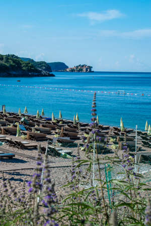 View of beautiful Kamenovo pebble beach location near Rafailovici village. Beach equipped with sun loungers and umbrellas. Resort Aman Sveti Stefan island backgound. Budva Riviera. Montenegro.の写真素材