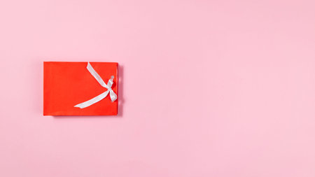 Gift red package bag decorated with a white ribbon on light pink background. Minimalistic concept of...
