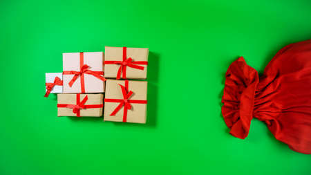 Gift boxes tied with a red ribbon are near the red sack of Santa Claus. Green background. Concept of holidays and gifts preparation. Flat lay. Copy space.の写真素材
