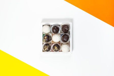 Square white box with round chocolate candies on a white background with yellow and orange accents. Sweet dessert concept. Copy spase. Flat lay.の写真素材