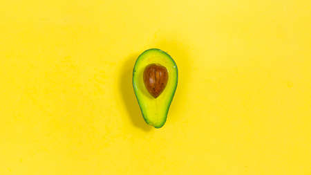 Half of a ripe avocado with a stone in the middle on a yellow background close-up. The concept of proper nutrition and healthy fruits.の写真素材