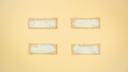 Four rectangular whole grain crisps are spread with white sauce and prepared for sandwiches. A healthy, nutritious yeast-free snack. Minimal healthy nutrition concept. flat lay.の写真素材