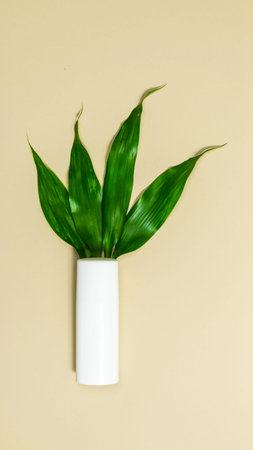 White tube with cosmetics cream on a beige background. Green leaves sprout from the tube. The...