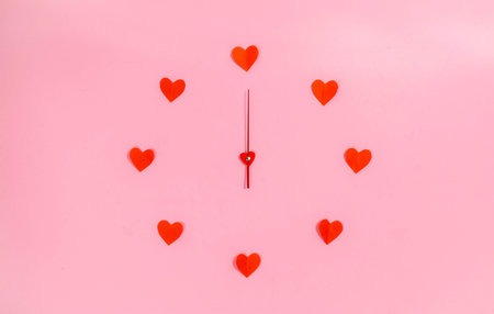 Clock hands in the center of a circle of red paper hearts. love time. copyspace. flat lay. pink...