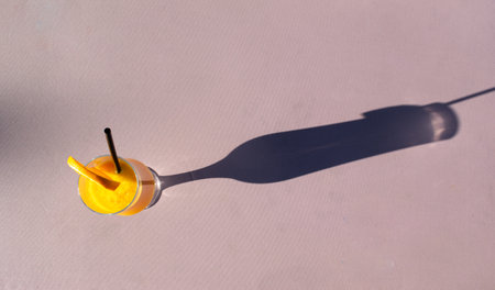 Glass of freshly squeezed orange juice with a straw and an orange slice casts a long, contrasting shadow on a fabric background. The concept of summer cocktails.の写真素材