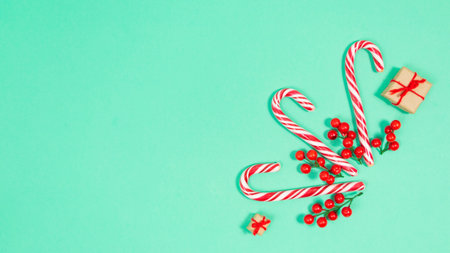 Candy canes are decorated with red berries and small gift boxes. Turquoise background. Beautiful...