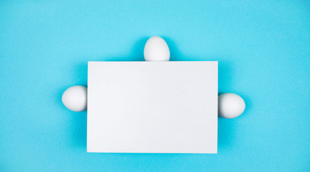 Three white chicken eggs behind a sheet of white paper. Happy Easter Day Concept. Light blue background. Holiday greeting card. Copy space. Template for text.の写真素材