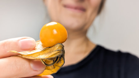 Ripe yellow physalis fruit berry close up against background of female face. Physalis peruviana, edible physalis species. Small golden berries. Vegetarian food. Experience of healthy lifestyle. White background.の写真素材