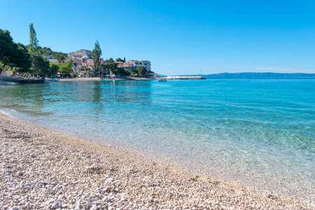 Serenely calm Adriatic Sea in summer season. Clean small-pebble beach early in the morning. Village of Promajna, Croatia. Houses at foot of foot on horizon. Vacation location.の写真素材